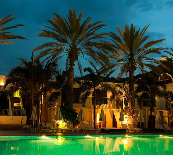 Piscina nocturna con el telón de fondo de palmeras y hoteles —  Fotos de Stock