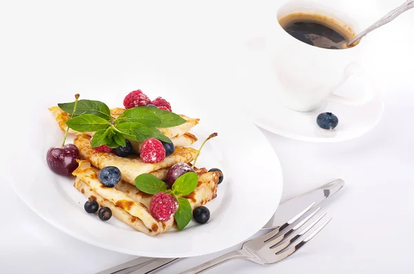 Млинці з ягодами, м'ятою та чашкою кави на білому фоні — стокове фото