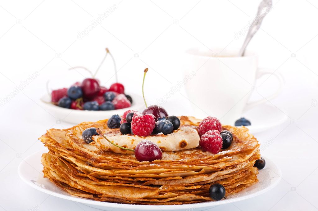 Pancakes with berries and cup of coffee on a white background