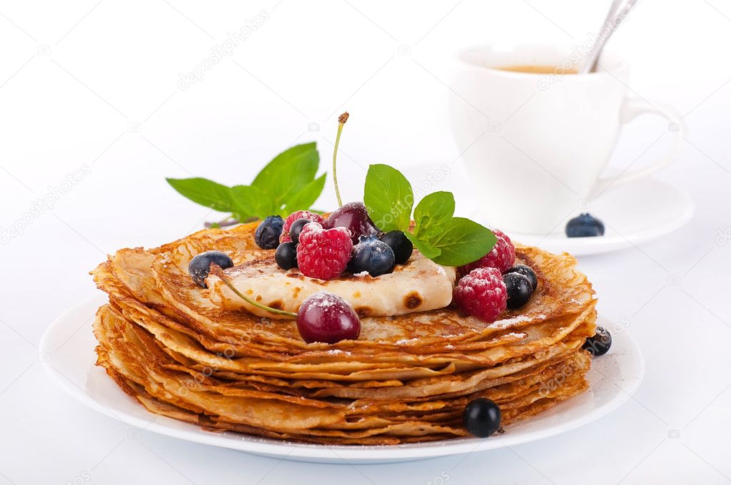 Pancakes with berries and mint and cup of coffee on a white background