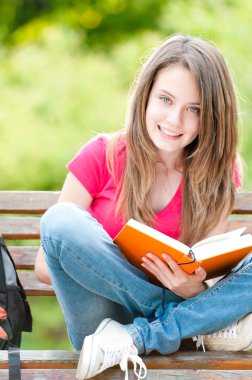 kitap ile bankta oturan mutlu öğrenci kız