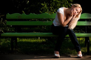 Parktaki bankta oturan üzgün genç kadın
