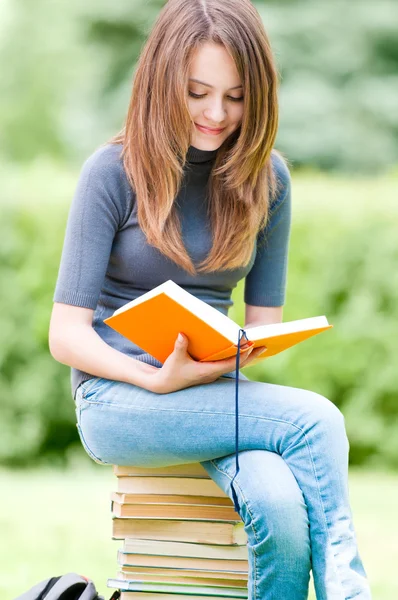 Heureuse étudiante assise sur une pile de livres — Photo