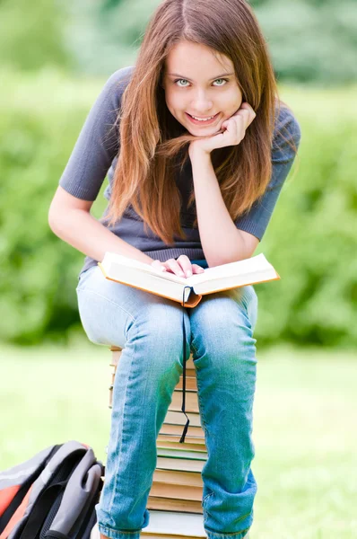 Glückliches Studentenmädchen auf Bücherstapel sitzend — Stockfoto