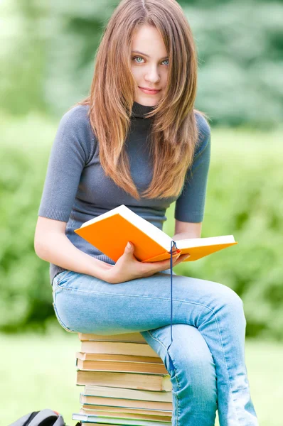 Счастливая студентка сидит на стопке книг — стоковое фото