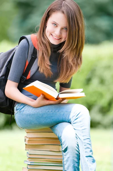 Happy student girl sitting on pile of books — Stock Photo, Image