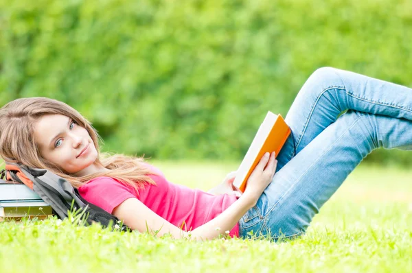 Menina estudante feliz deitado na grama com livro aberto — Fotografia de Stock