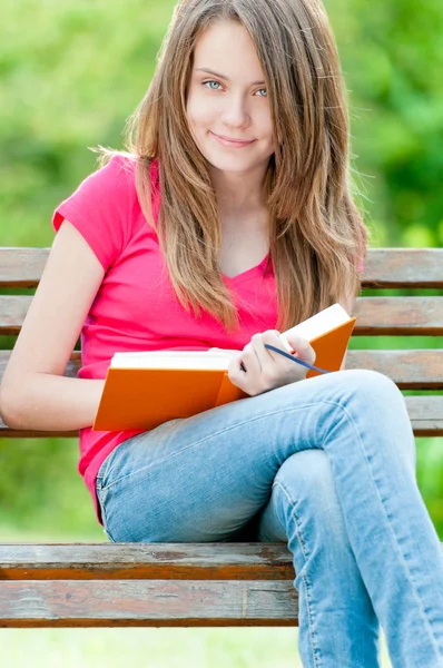 Menina estudante feliz sentado no banco com livro — Fotografia de Stock