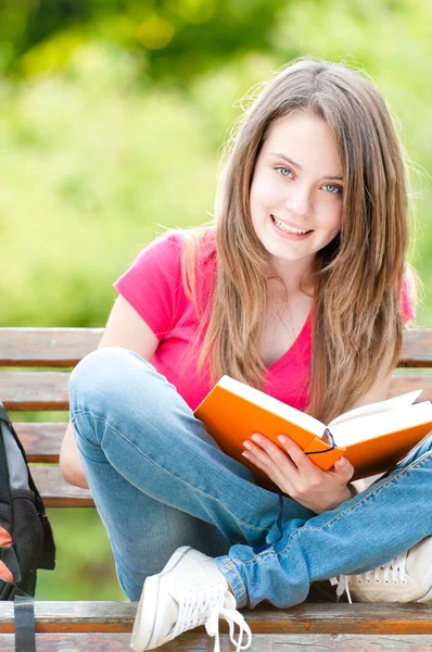 Kitap ile bankta oturan mutlu öğrenci kız — Stok fotoğraf