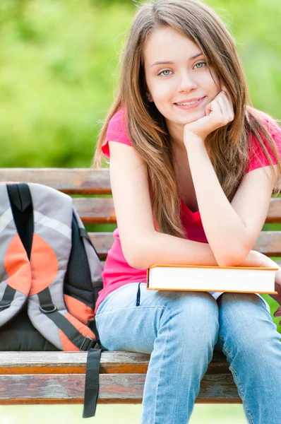 Happy student girl sitting on bench with book — Stock Photo, Image