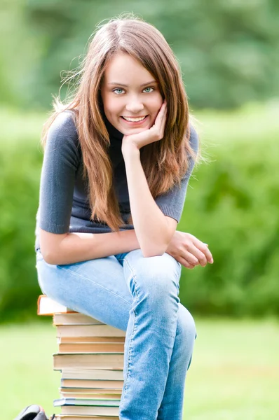 Счастливая студентка сидит на книгах — стоковое фото