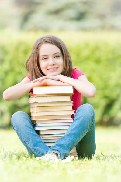 Glückliches Studentenmädchen, das neben einem Stapel Bücher sitzt — Stockfoto