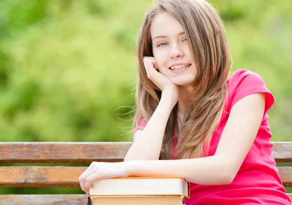 Счастливая студентка сидит на скамейке с книгами и улыбается — стоковое фото