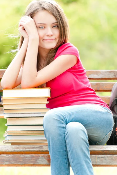 Счастливая студентка сидит на скамейке с кучей книг — стоковое фото
