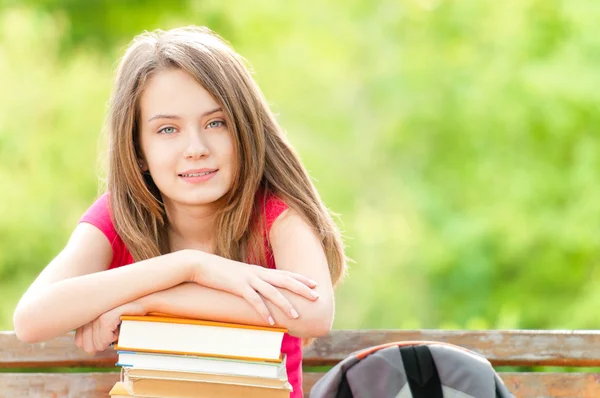 Chica estudiante feliz sentado en el banco con libros y sonriendo —  Fotos de Stock