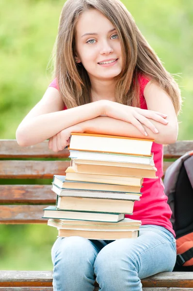 Boldog diák lány ül a padon, a könyvek, és mosolyogva — Stock Fotó