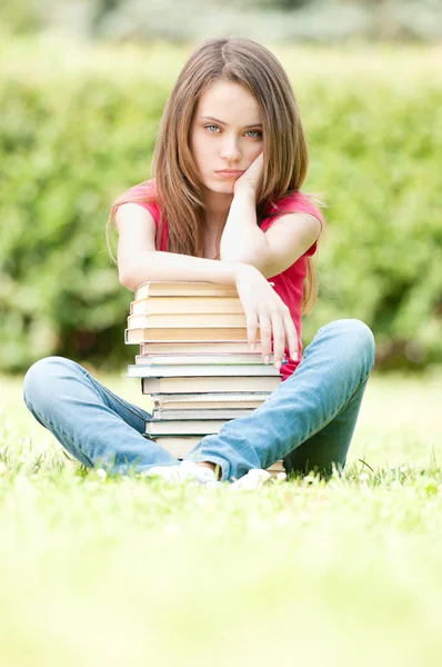 Грустная студентка сидит рядом с грудой книг — стоковое фото
