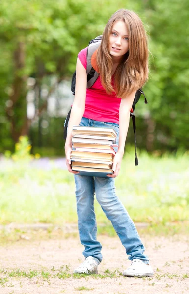 Молодая студентка с большой грудой тяжелых книг — стоковое фото