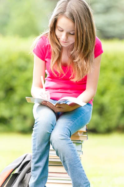 Genç öğrenci kız kitap yığınının üzerinde oturuyordu — Stok fotoğraf