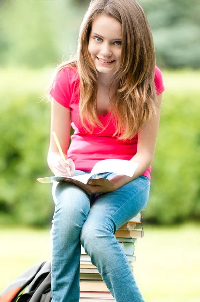 Jovem estudante sentada na pilha de livros — Fotografia de Stock