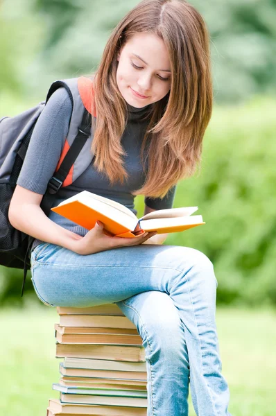 Jovem estudante sentada na pilha de livros — Fotografia de Stock