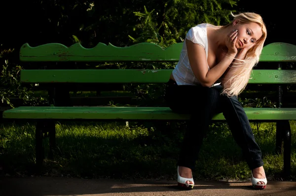 Sad young woman sitting on bench in park — Stock Photo, Image