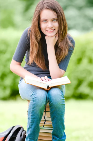 Ευτυχής φοιτητής κορίτσι που κάθεται στο σωρό των βιβλίων Εικόνα Αρχείου