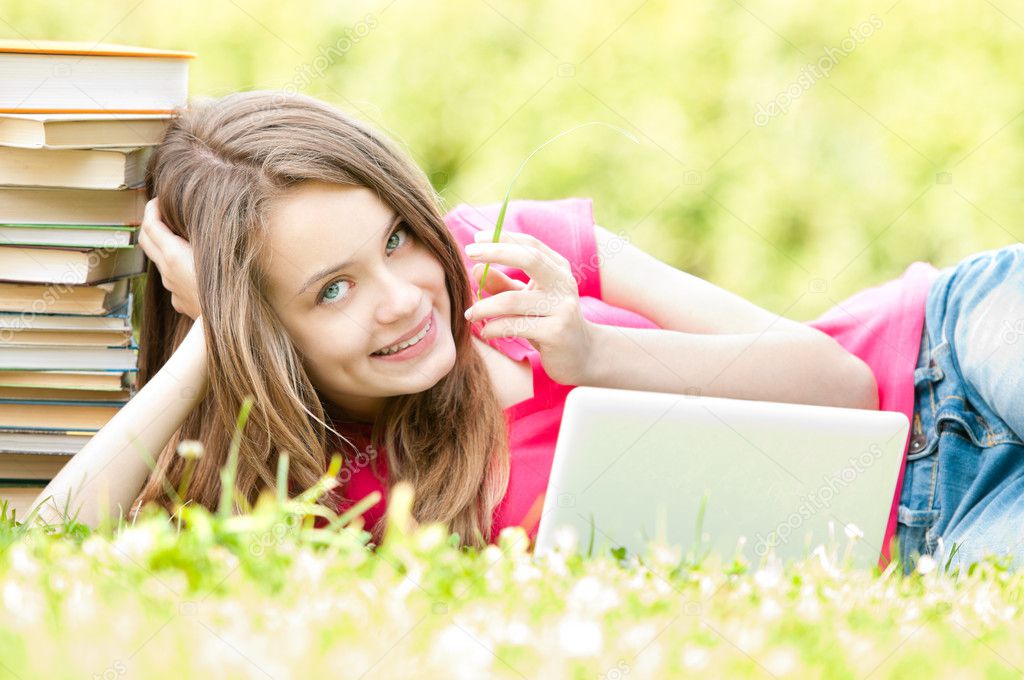 Happy student girl lying on grass with laptop computer