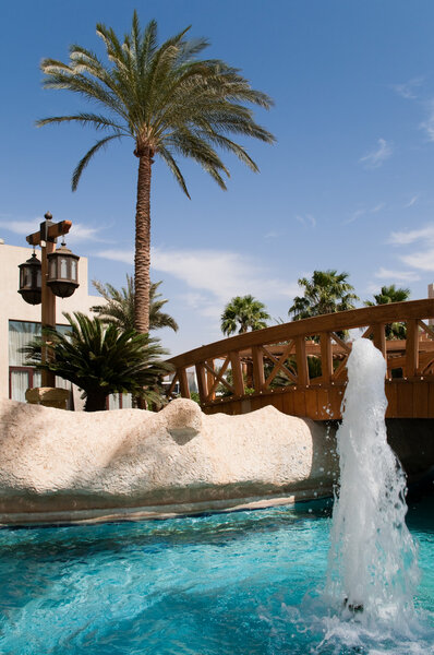 Hotel pool with fountain, bridge over the pool and blue sky in background