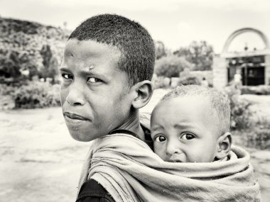 An Ethiopian boy carries his little brother on his back clipart