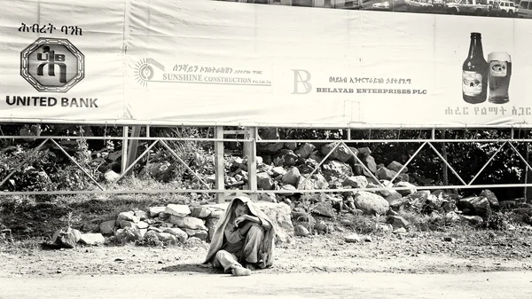 Un hombre etíope se sienta en el suelo bajo la bandera de la promoción — Foto de Stock