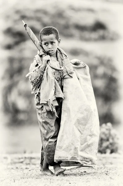 Um menino etíope carrega um guarda-chuva e outras coisas — Fotografia de Stock