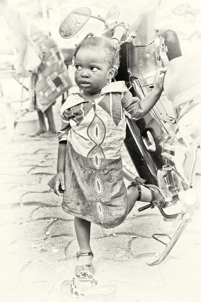 Piccola ragazza del Benin posa per la fotocamera vicino a una moto — Foto Stock