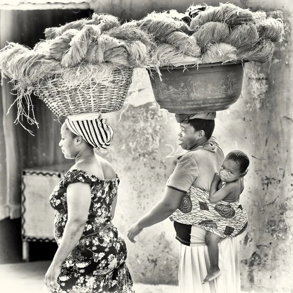 Two Ghanaian ladies carry the stuff on their heads and one of them carries the baby on the back as well