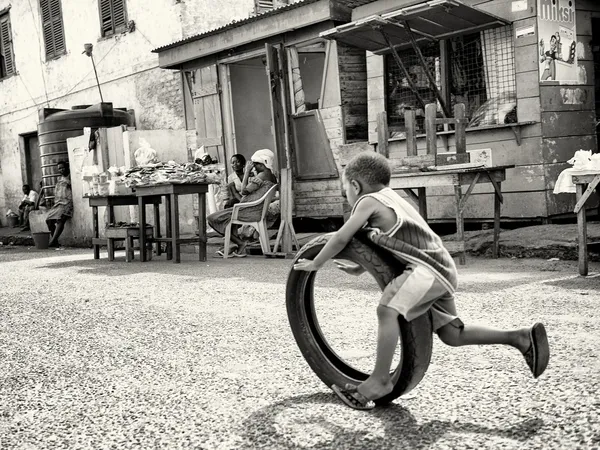 El pequeño chico ghanés juega con un neumático y su madre lo mira —  Fotos de Stock