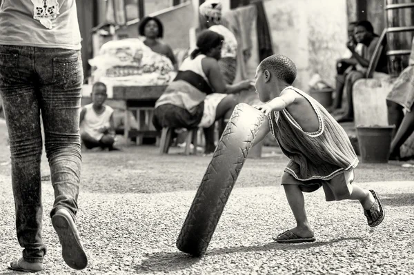 Liten Ghanansk pojke går och leker med ett däck — Stockfoto