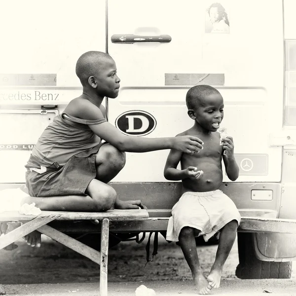 A Ghanaian boy eats something and an other boy wants to try it as well — Stock Photo, Image