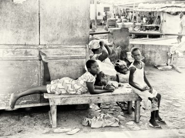 Two Ghanaian boys sit on a bench near the market clipart