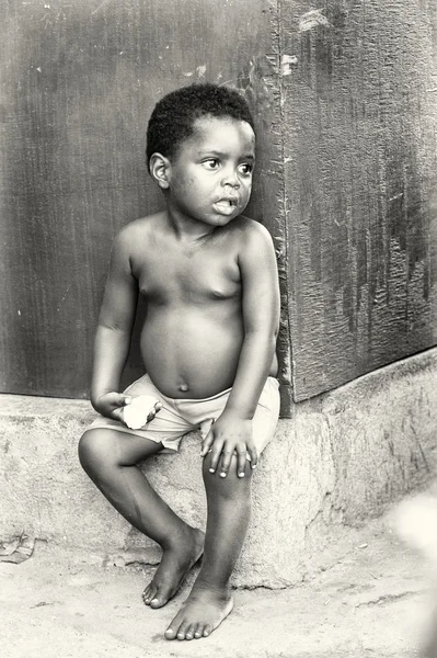 Pequeno menino ganês senta-se e come — Fotografia de Stock