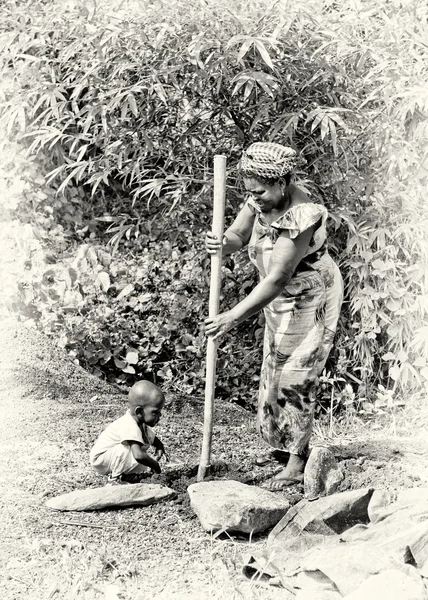 Eine ghanaische Dame gräbt und ihr Baby schaut zu — Stockfoto