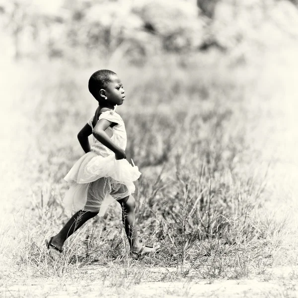 白いドレスを着たガーナ女の子はフィールドを介して実行します。 — ストック写真