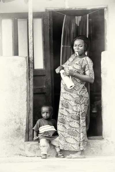 Ein kleiner Junge sitzt vor der Tür und seine Mutter bleibt neben ihm mit einem Teebeutel — Stockfoto