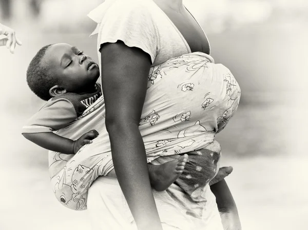 Ein kleiner ghanaischer Junge schläft, während er von seiner Mutter auf dem Rücken getragen wird — Stockfoto