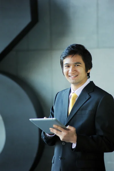 Ασιατικός επιχειρησιακός άνθρωπος ντυμένος με κοστούμι και γραβάτα, χαμογελώντας με δισκίο Royalty Free Φωτογραφίες Αρχείου