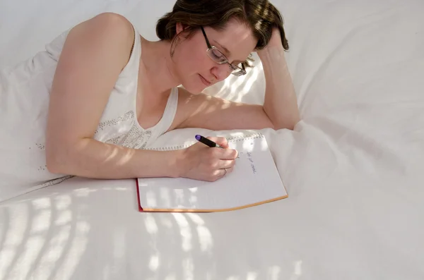 Mujer en una cama escribiendo notas — Foto de Stock