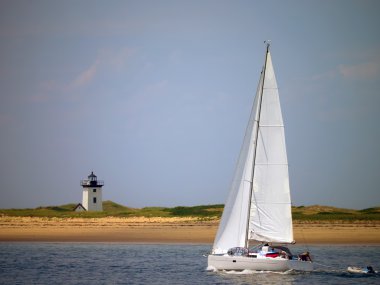 White sailboat off the coast of Cape Cod with lighthouse in background clipart