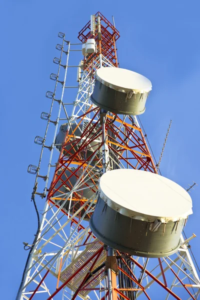 Telekommunikationen står hög med antenner en blå himmel. Stockbild