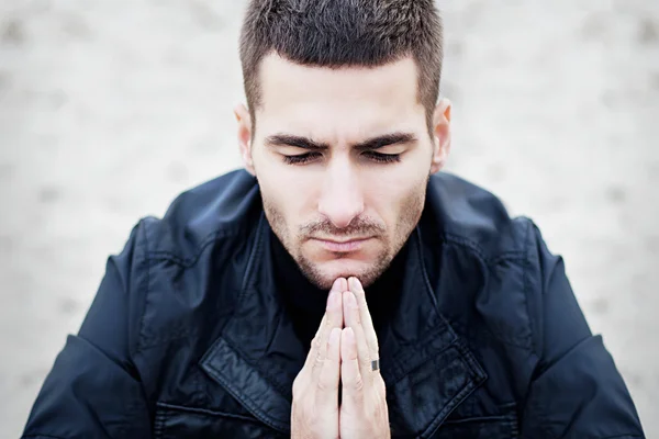 Praying man in dark clothing on a light background