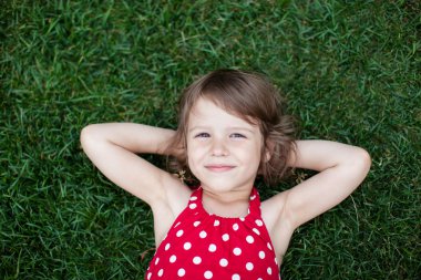 Portrait of a smiling little girl lying on green grass clipart