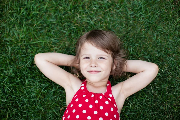 一个微笑的小女孩躺在绿草上的画像 — 图库照片